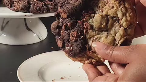 Load video: Video of various baked cookies displayed on a cake stand. One of the chocolate chip cookies is broken in half showing a warm